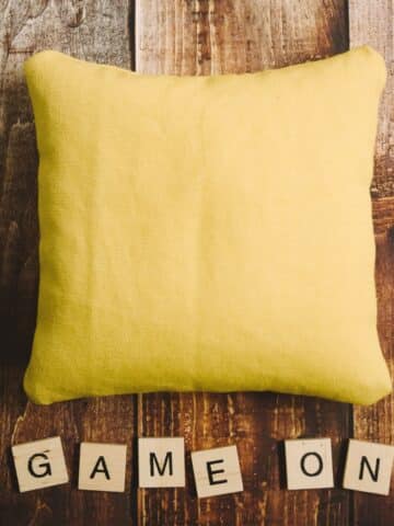 Yellow DIY cornhole bag and scrabble tiles that say "game on".