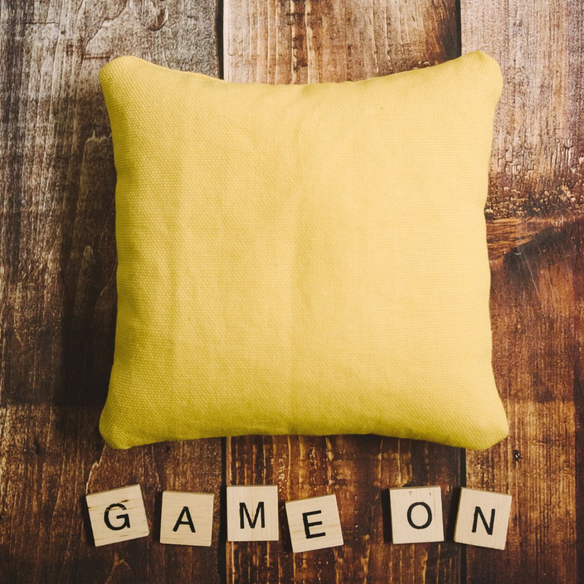 Yellow DIY cornhole bag and scrabble tiles that say "game on".