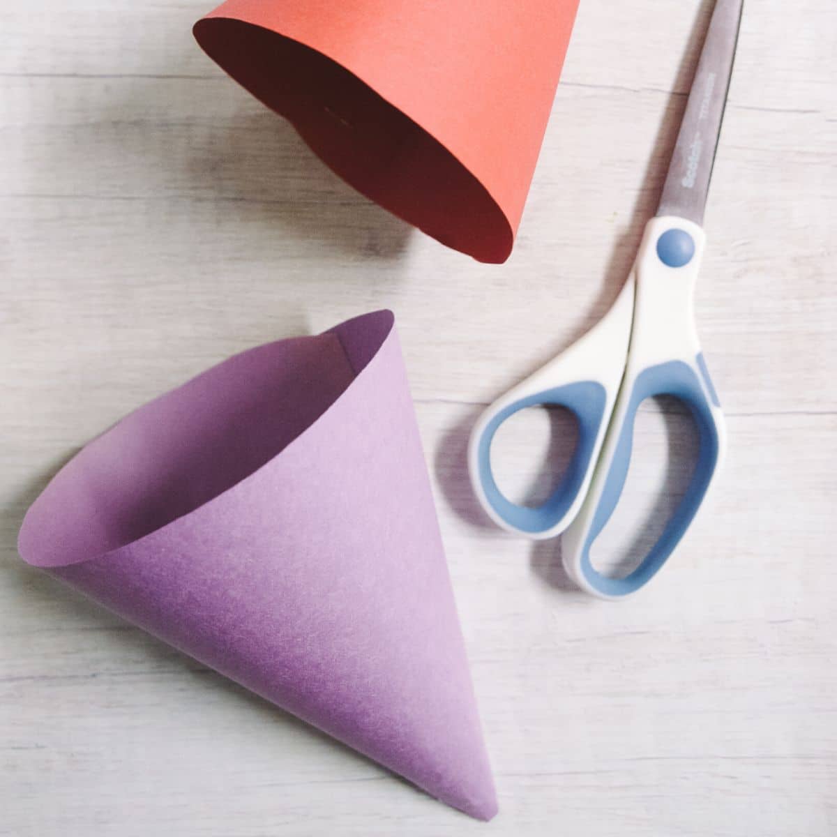 Purple and red paper cones made with construction paper, laying with a scissors on a table top.