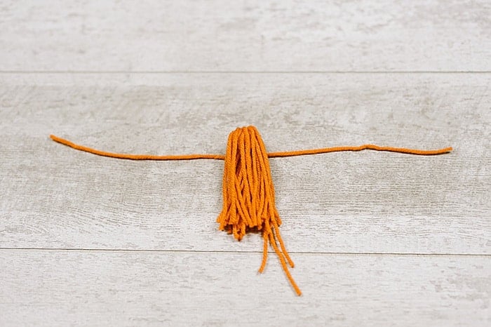 lay a 10 inch piece of yarn down, lay the tassel bundle on top