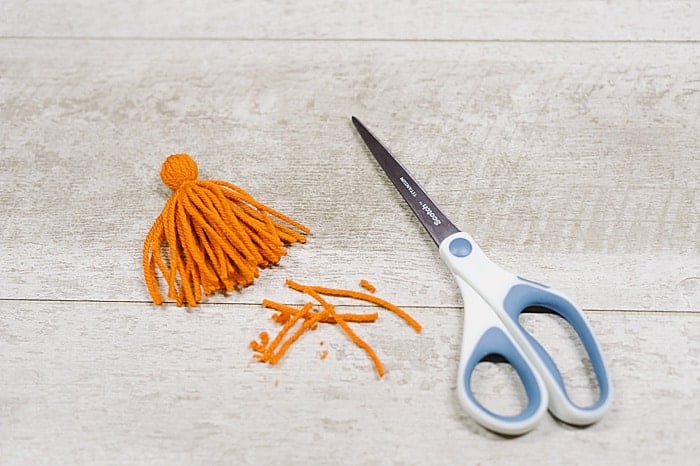 Scissors trimming up the bottom of a yarn tassel.