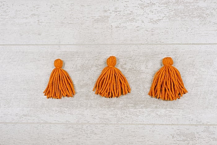 Three yarn tassels of different thicknesses laying on a flat surface.
