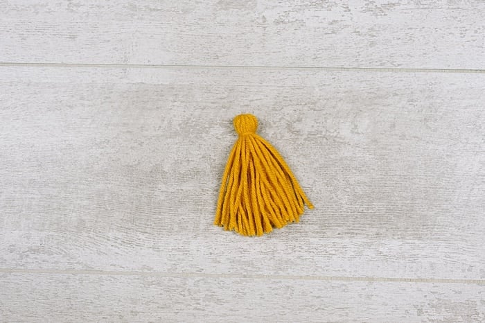 A yarn tassel laying on a wood surface.