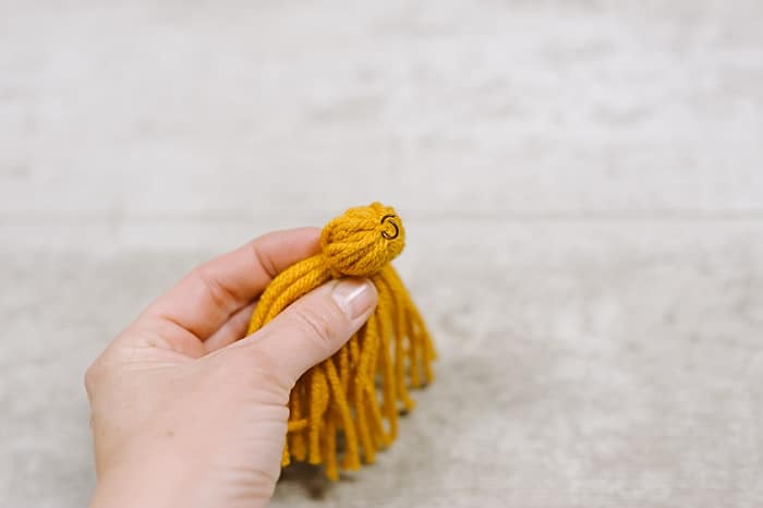 slide a metal jump ring under the tie string at the top of the diy yarn tassel