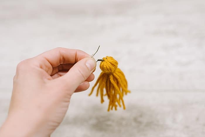 slide the open earring hook under the tie string at the top of the tassel