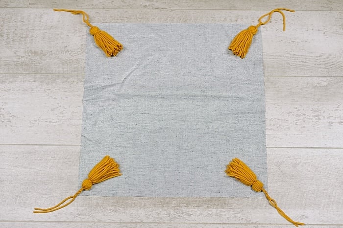 lay fabric out and add one tassel to each corner, facing IN