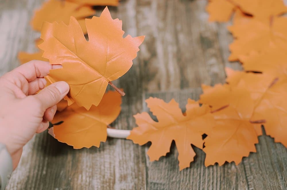 Hot gluing leather leaves onto a wreath form to make a fall leaf wreath.