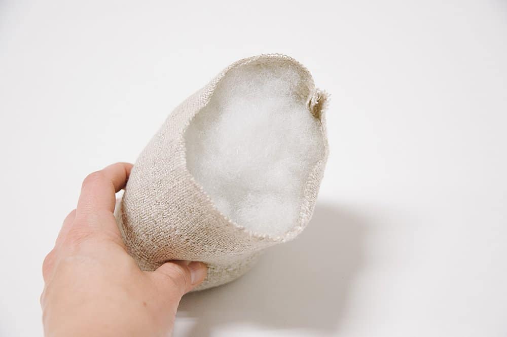 A linen fabric tube being stuffed with poly fil.