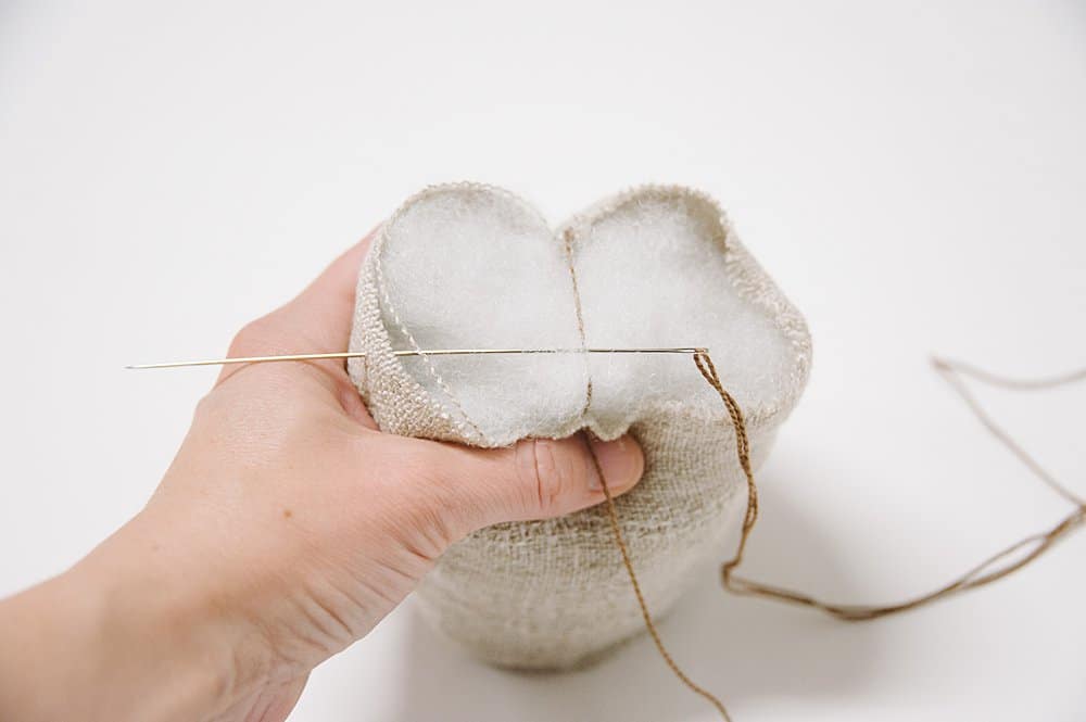 Sewing linen fabric with an embroidery needle and embroidery floss to make a fabric pumpkin.