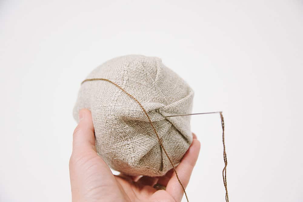 Sewing linen fabric with an embroidery needle and embroidery floss to make a fabric pumpkin.