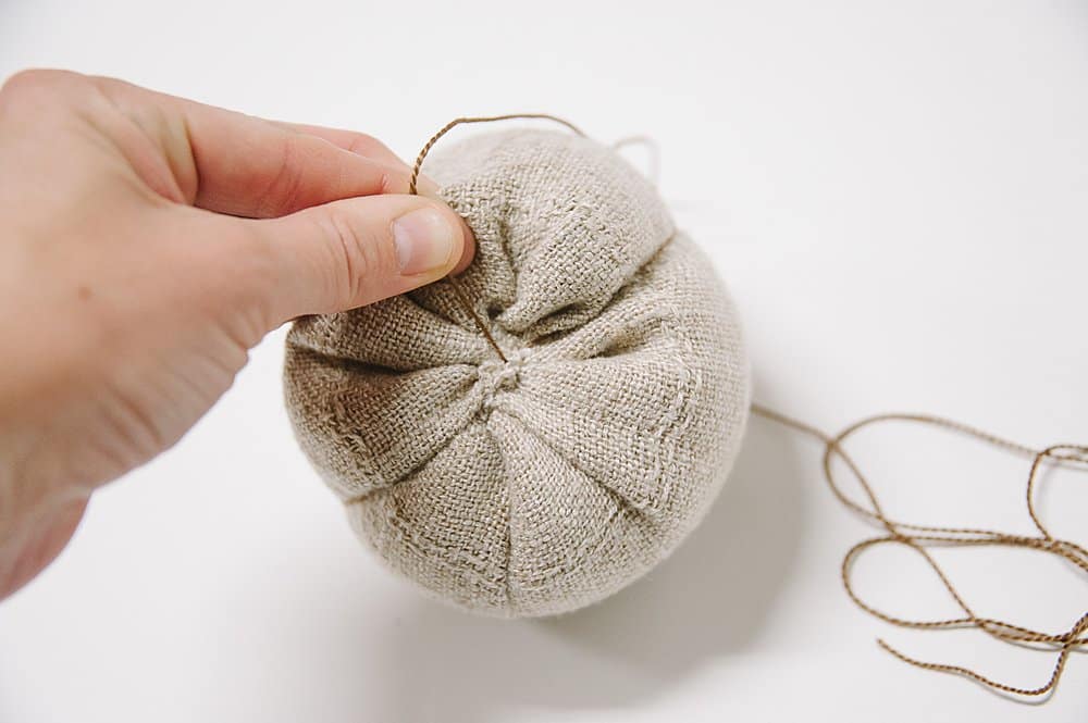 Sewing linen fabric with an embroidery needle and embroidery floss to make a fabric pumpkin.