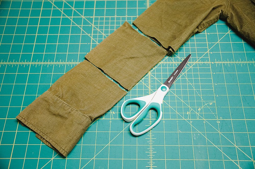 The sleeve of a green corduroy shirt being cut off to turn into a fabric pumpkin.
