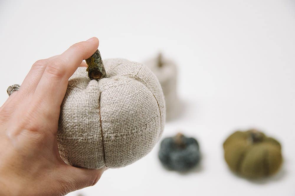 A wooden branch stem being hot glued onto a fabric pumpkin. 