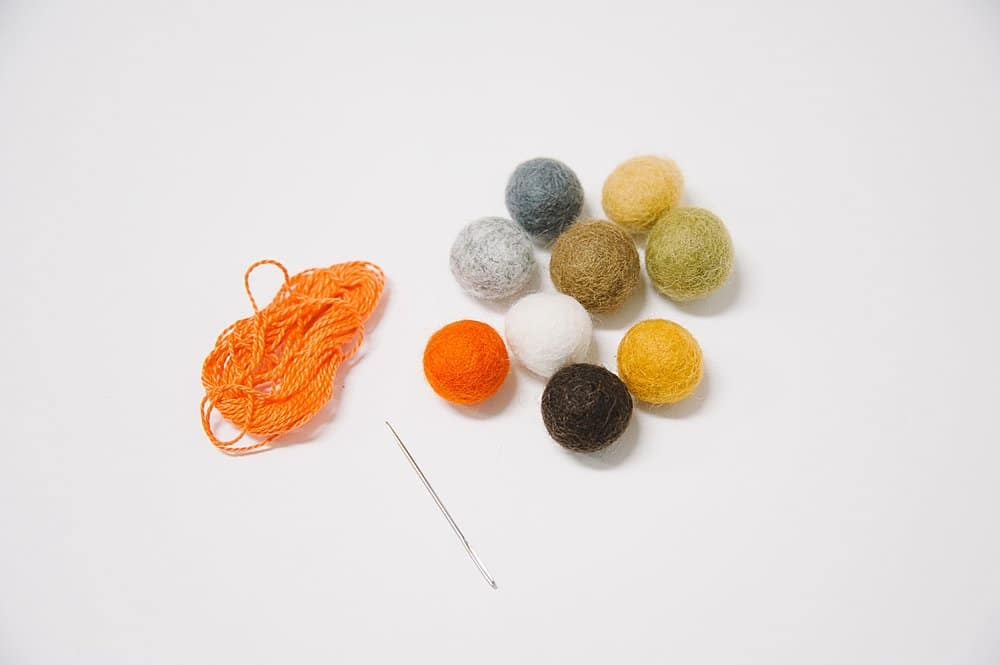 Supplies needed to make felt ball pumpkins - felt balls, embroidery floss, and an embroidery needle.