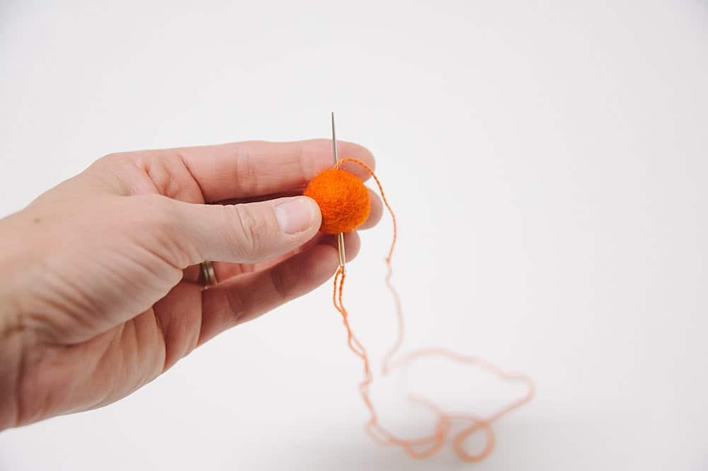 A needle and thread being pushed through the center of a felt ball to make a pumpkin.