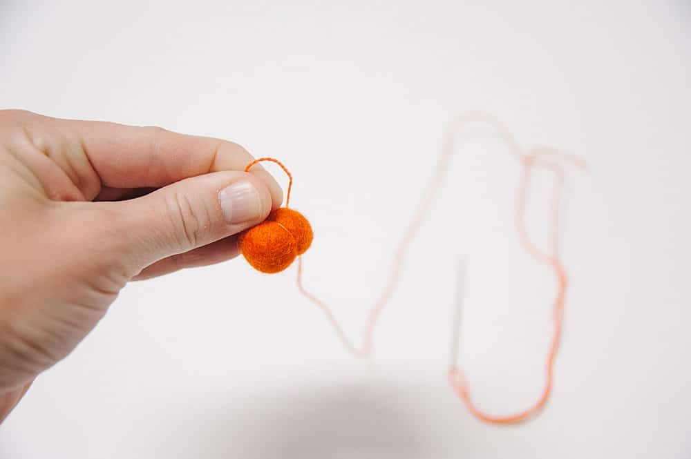 Embroidery floss making an indentation in the side of a felt ball to make it look like a pumpkin.