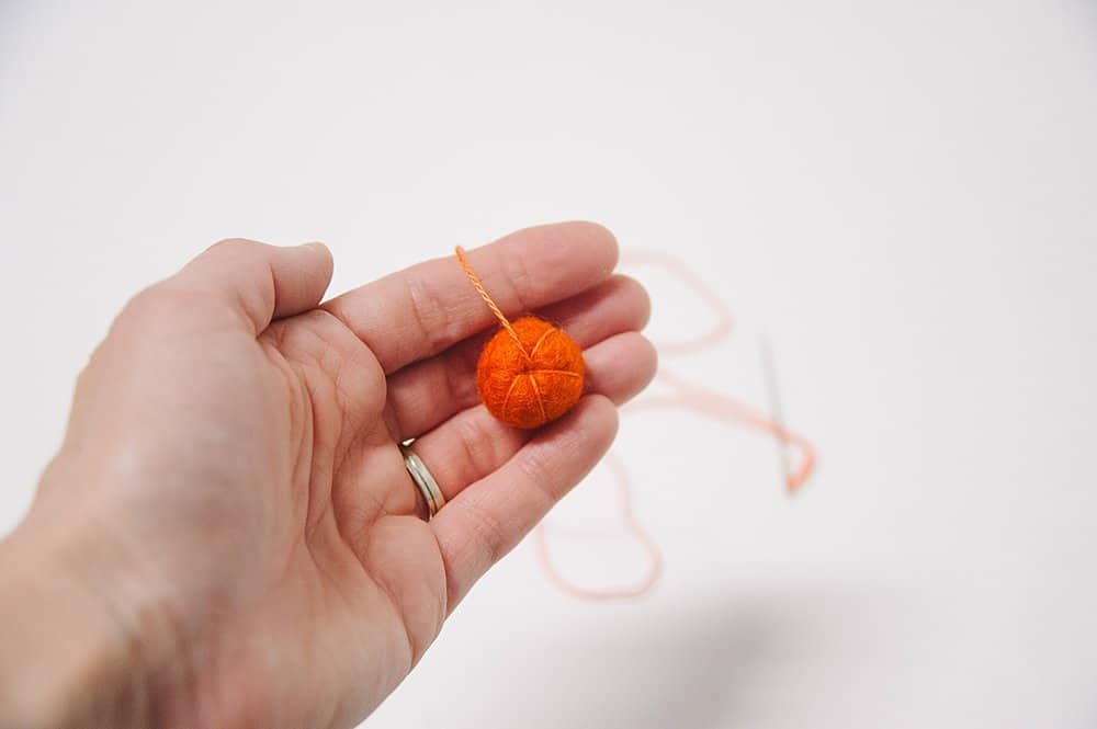 Using embroidery floss to make indentations in a felt ball like a pumpkin.