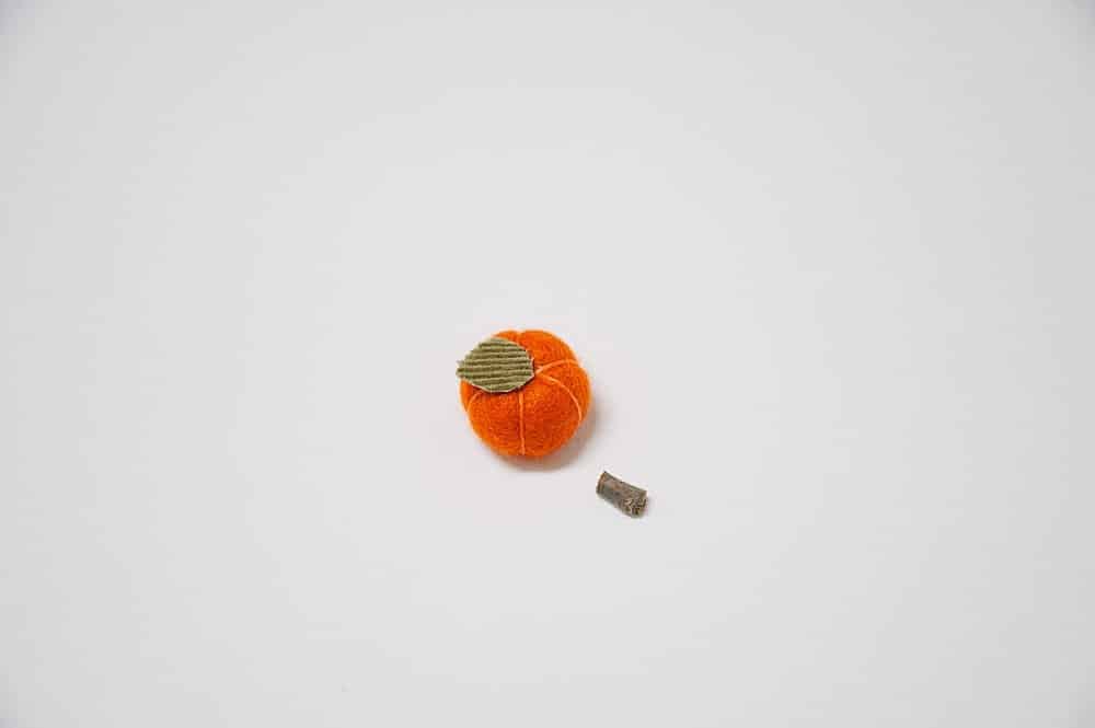 A small felt ball pumpkin with a green fabric leaf on top.