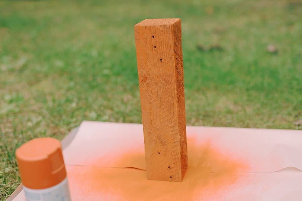 A section of wood being spray painted orange.