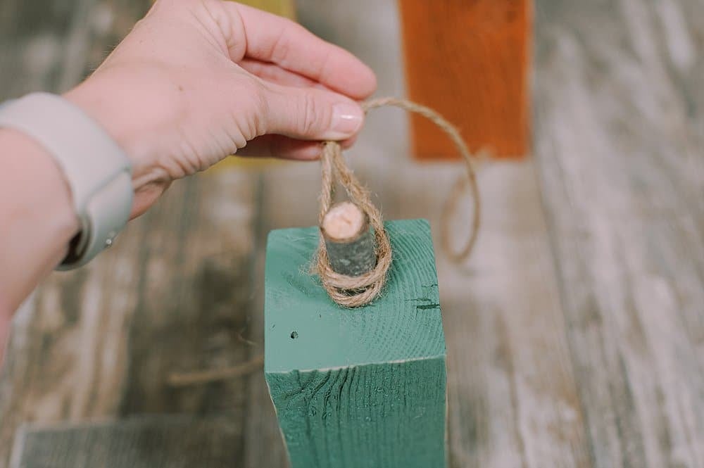 Wrapping twine around the a piece of tree branch glued as a stem to the top of a wooden block pumpkin.