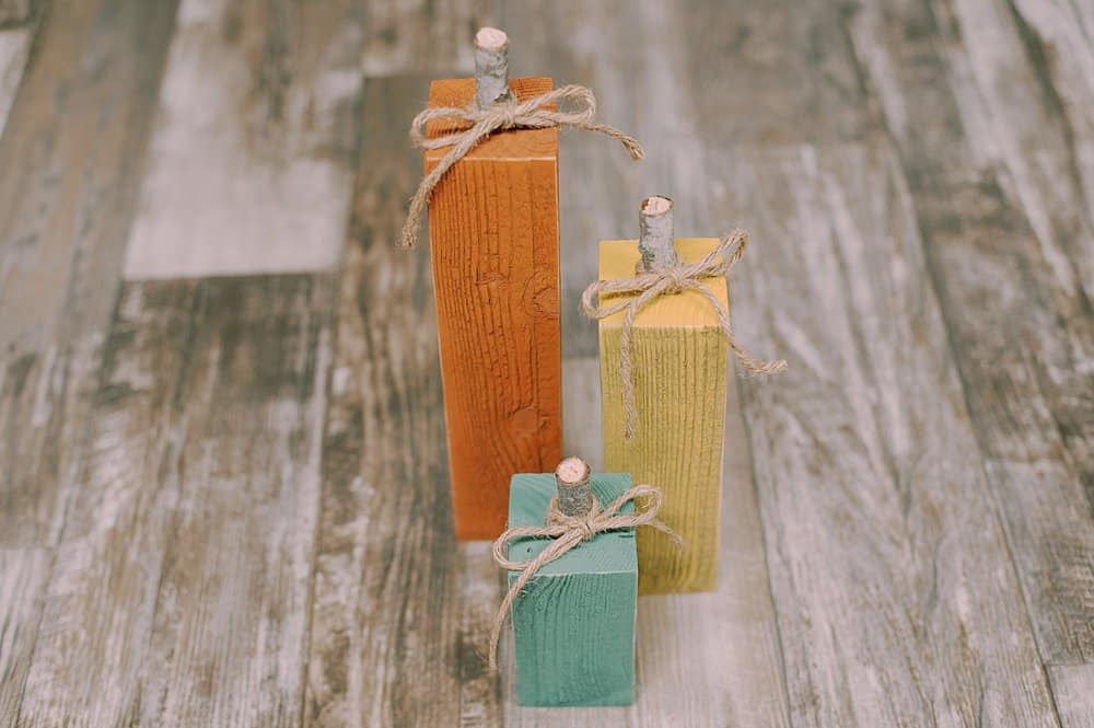 Orange, yellow, and green wooden pumpkins with stick stems and twine wrapped around the tops.