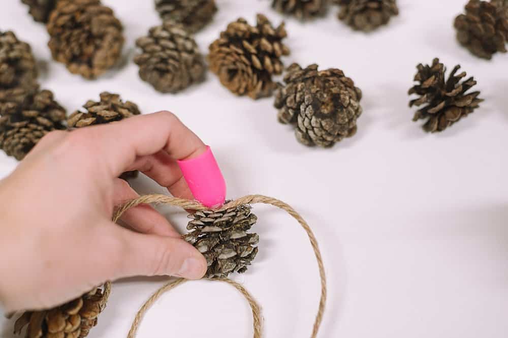 Use a silicone finger protector to hold the twine into the pinecone until the hot glue dries.