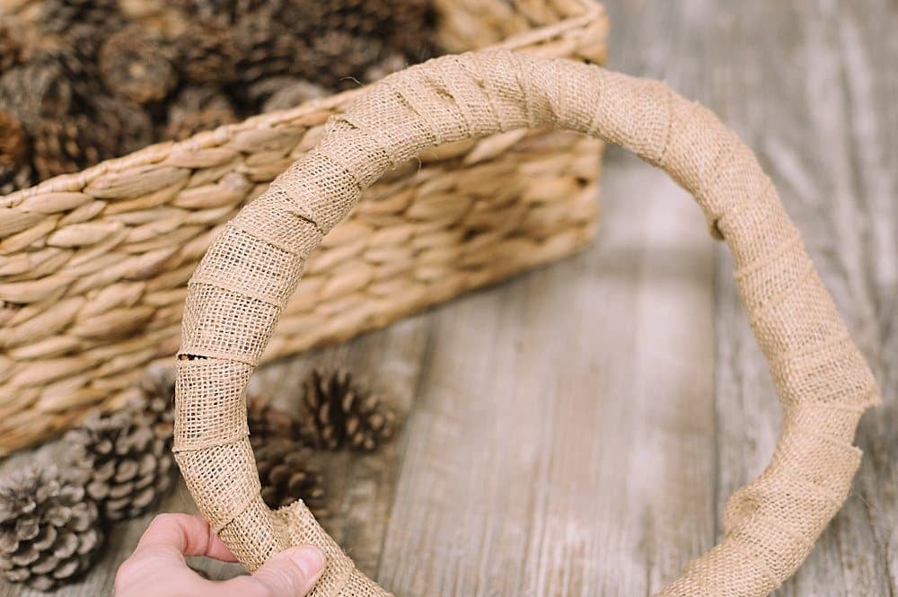A grapevine wreath, wrapped in burlap, ready to hot glue pinecones on them.