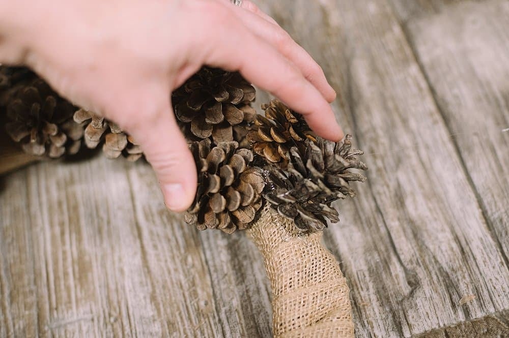 Hot glue pinecones to the burlap wrapped wreath form, and hold until the glue dries.
