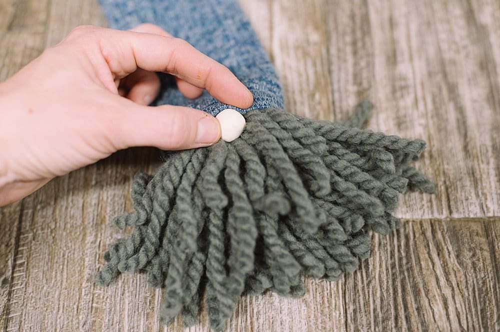 A painted clay nose gets hot glued onto the front of a yarn and sock gnome.