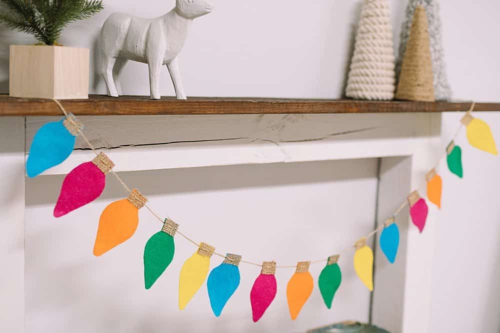 A colorful felt lightbulb garland hanging from a wood mantel.