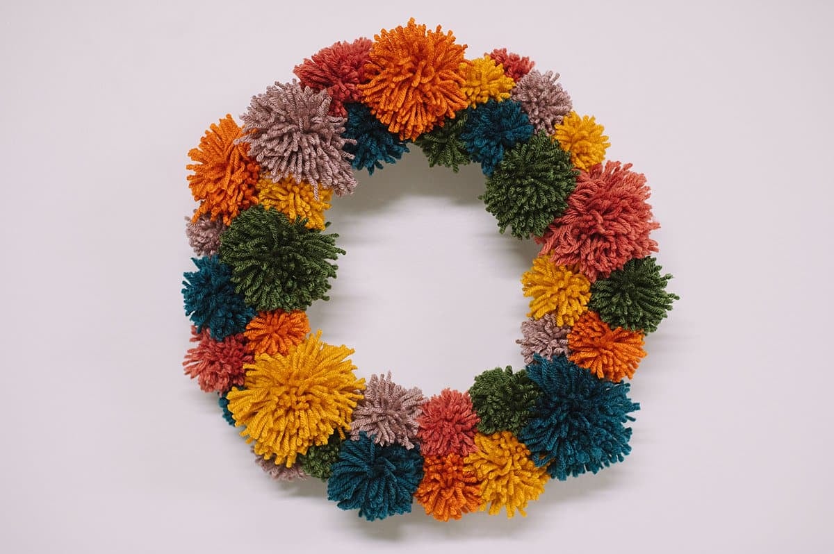 A pom pom wreath in rainbow colors, made with yarn.