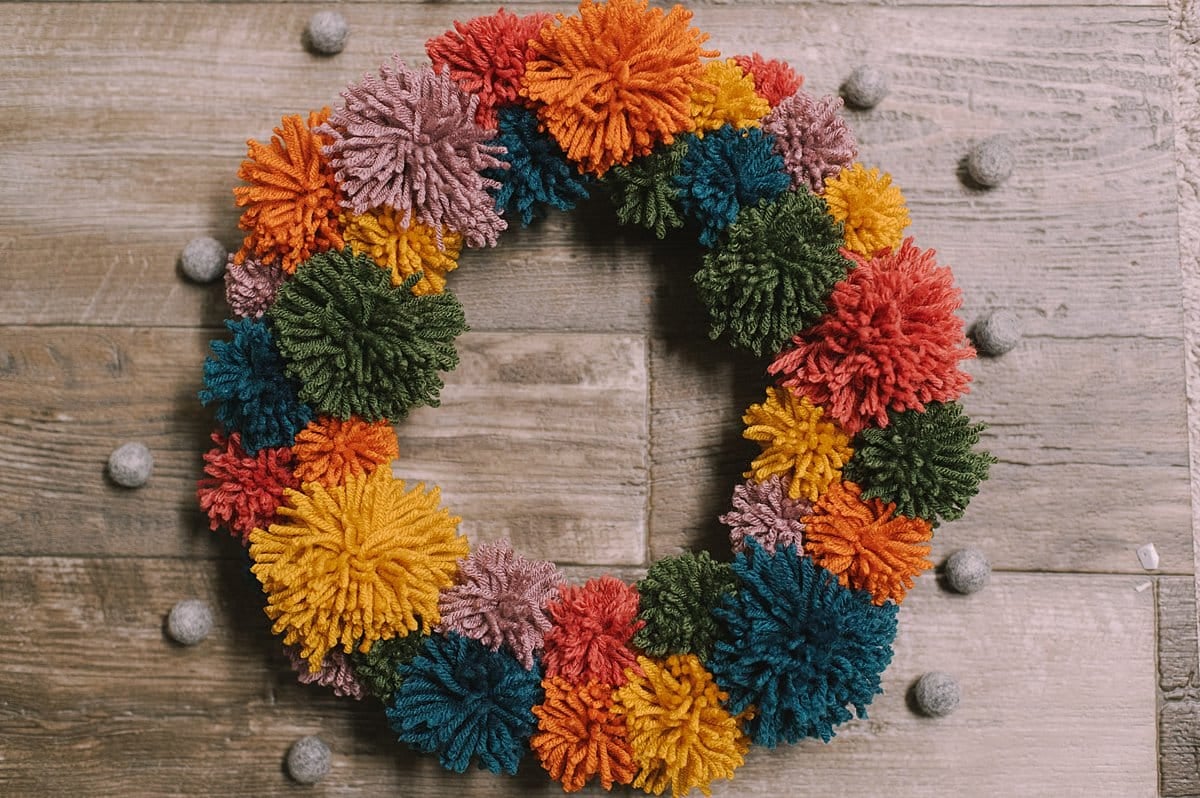 A yarn pom pom wreath made with rainbow colors.