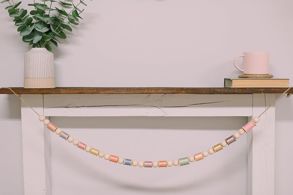 A spring wood bead and thread spool garland hanging on a mantel.