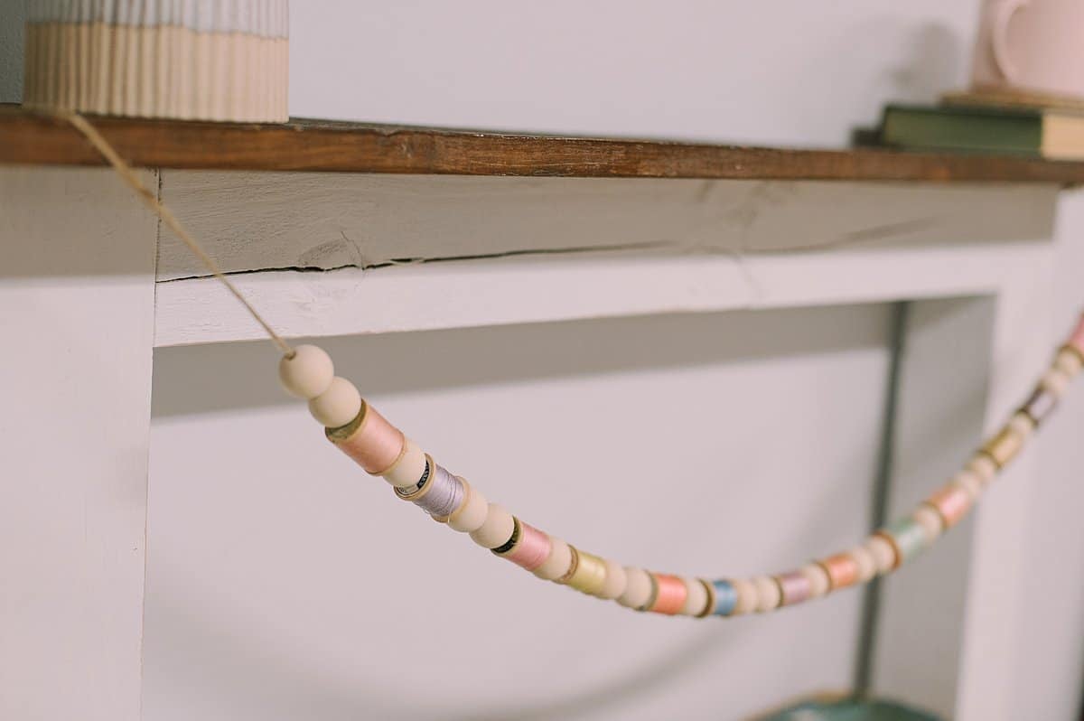 A springtime garland hanging on a mantel, made with wood beads and vintage thread spools.