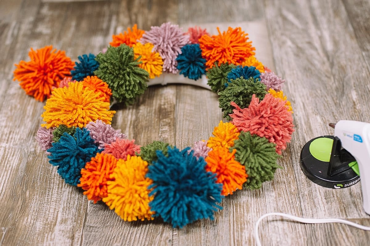 Hot glue pom poms onto styrofoam wreath.