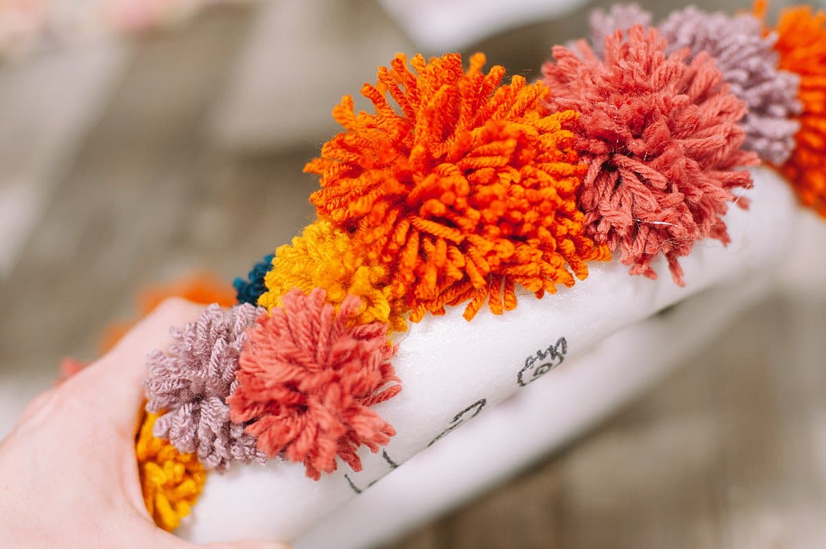 hot glue pom poms onto wreath form