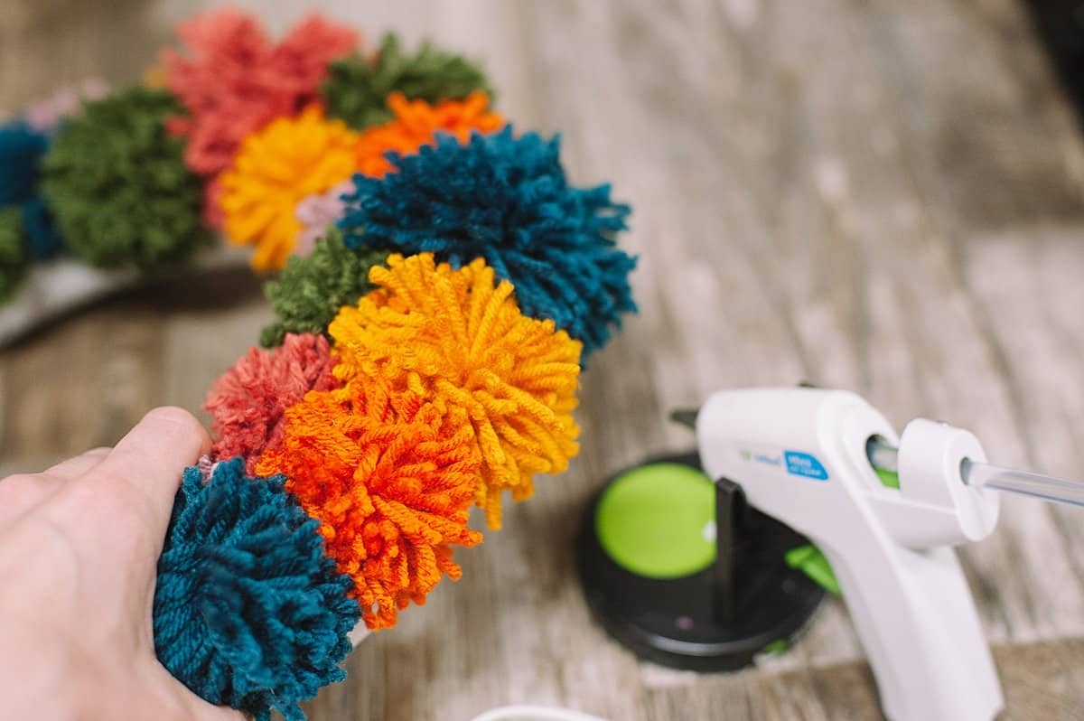 Hot glue pom poms onto the edge of a styrofoam wreath form.