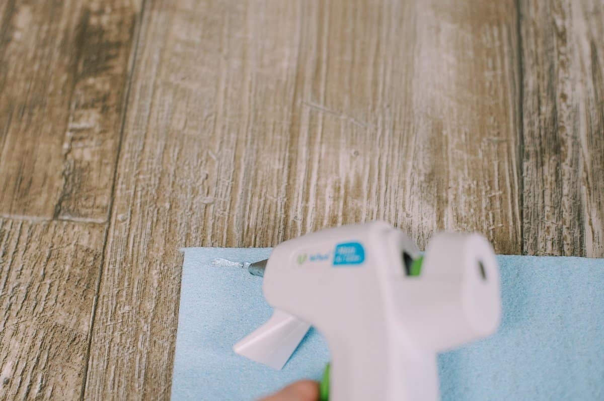 A hot glue gun putting a line of glue along the top of a felt rectangle.