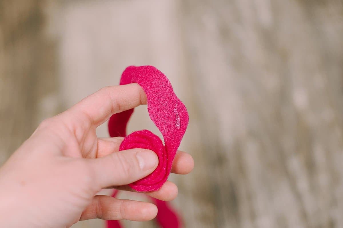 A hand holding felt and hot gluing it into a rosette shape.