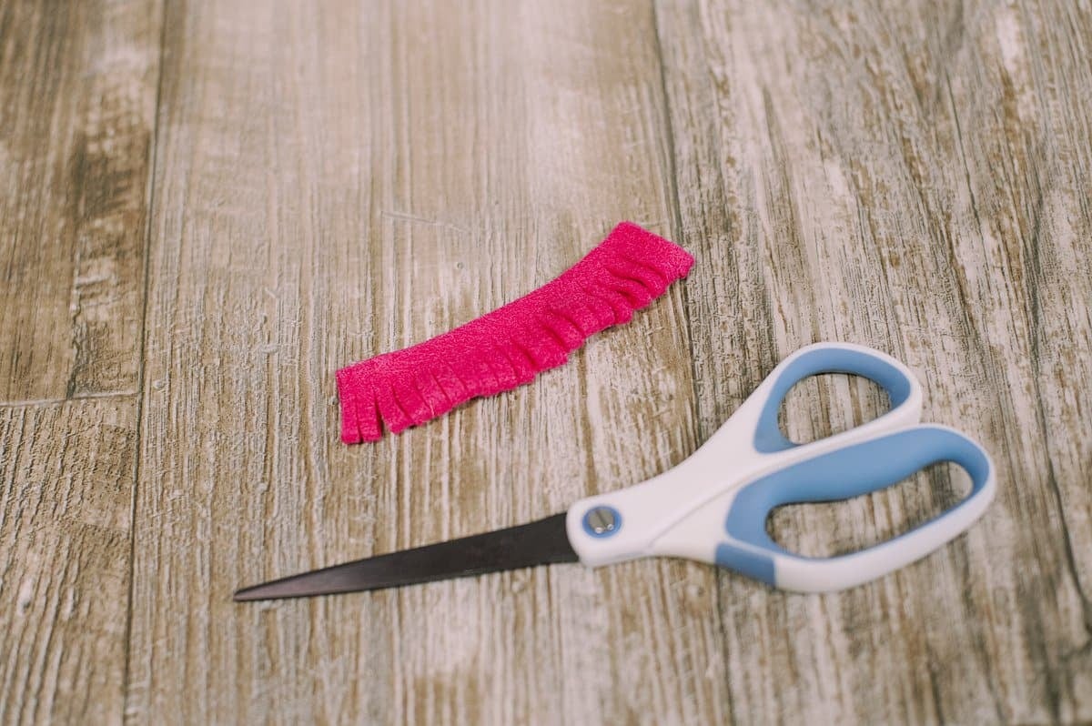 A fringed felt strip laying next to a scissors.