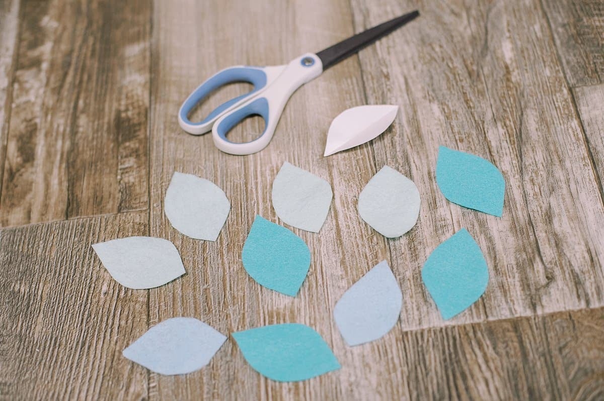 Felt flower petals laying on a flat surface alongside a scissors.