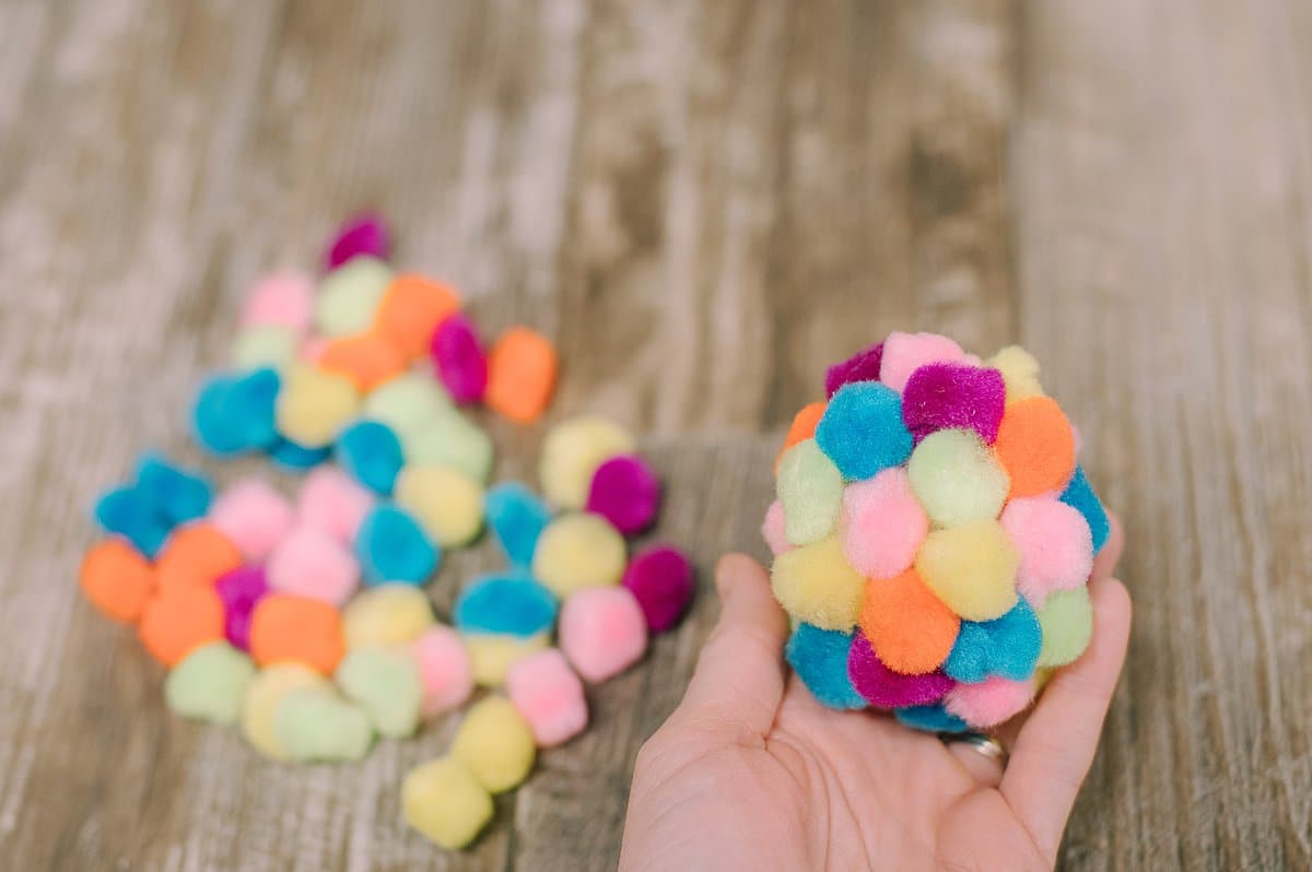 vary the color of pom poms and keep gluing until the whole plastic easter egg is covered