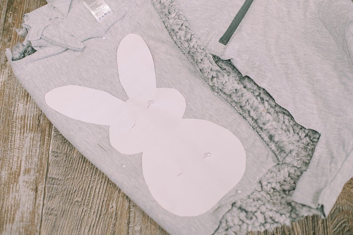 Paper bunny laying on top of folded fabric from an old sweatshirt, pinned into place.