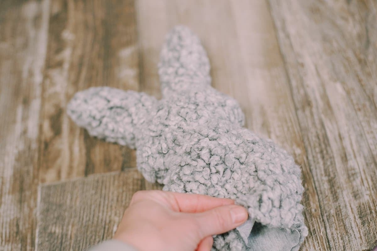 A fabric bunny being stuffed with poly-fil by hand.