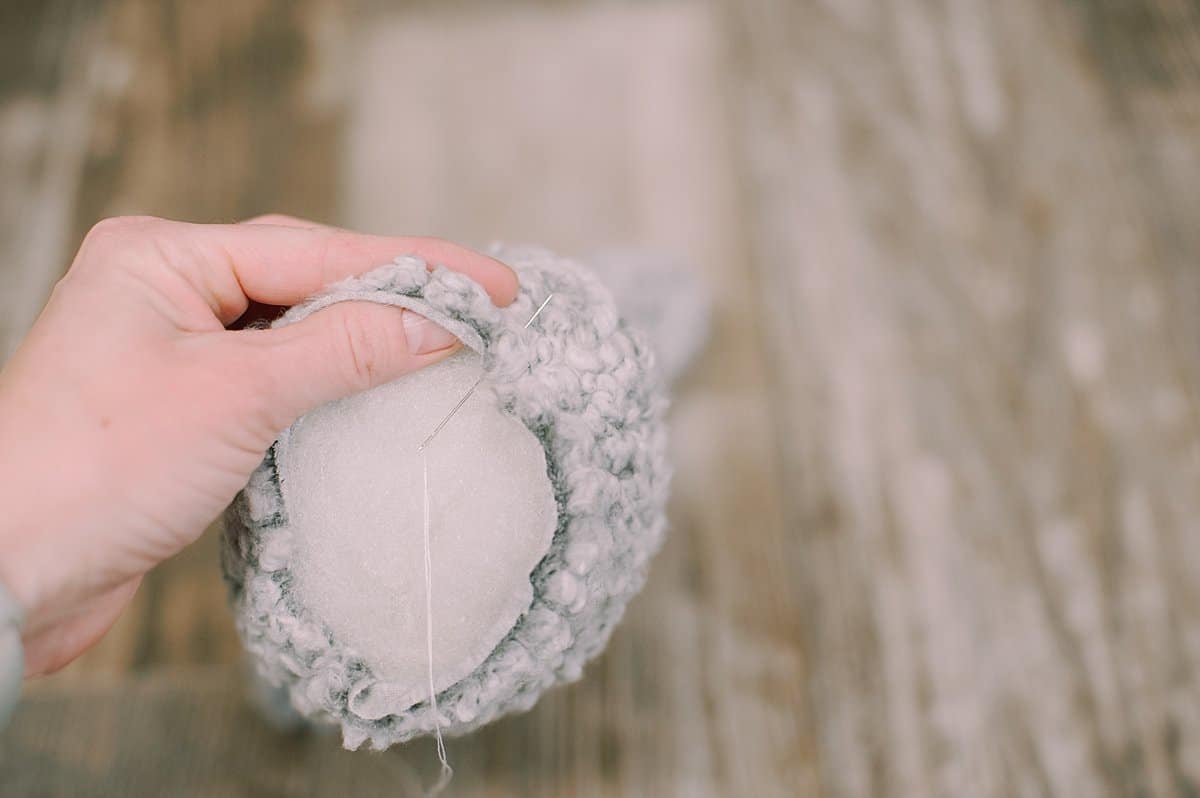 A hand holding a fabric bunny that is stuffed with poly-fil, and sewing the bottom up with a needle and thread.