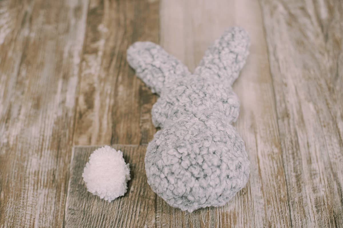 A handmade bunny-shaped stuffed animal with a white yarn pompom laying next to it.