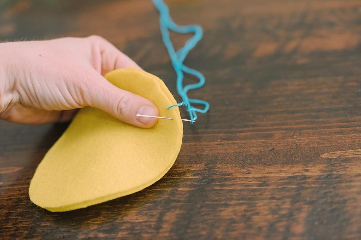 A hand holding egg shaped felt and stitching the outside edge with a needle and thread, doing the blanket stitch.