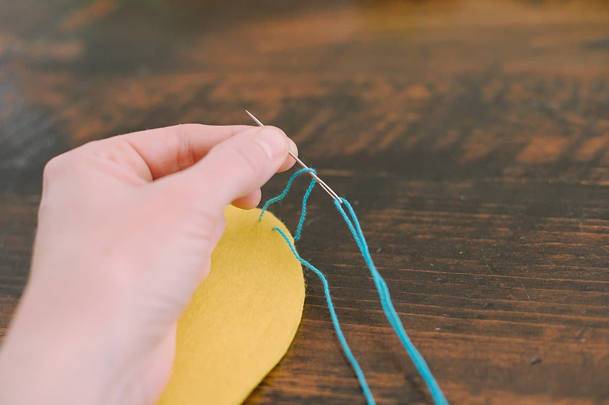 A hand holding egg shaped felt and stitching the outside edge with a needle and thread, doing the blanket stitch.