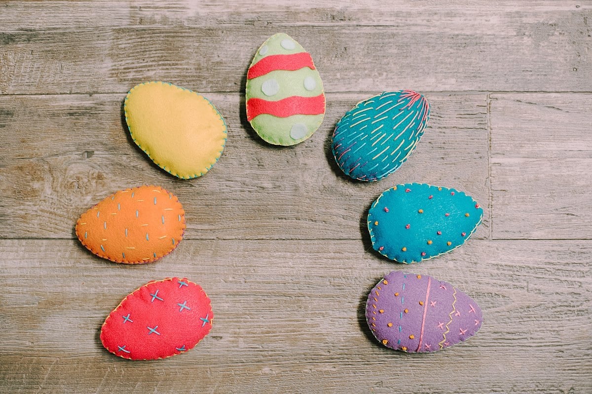 Multi-colored felt eggs with decorated fronts laying in an arch shape.