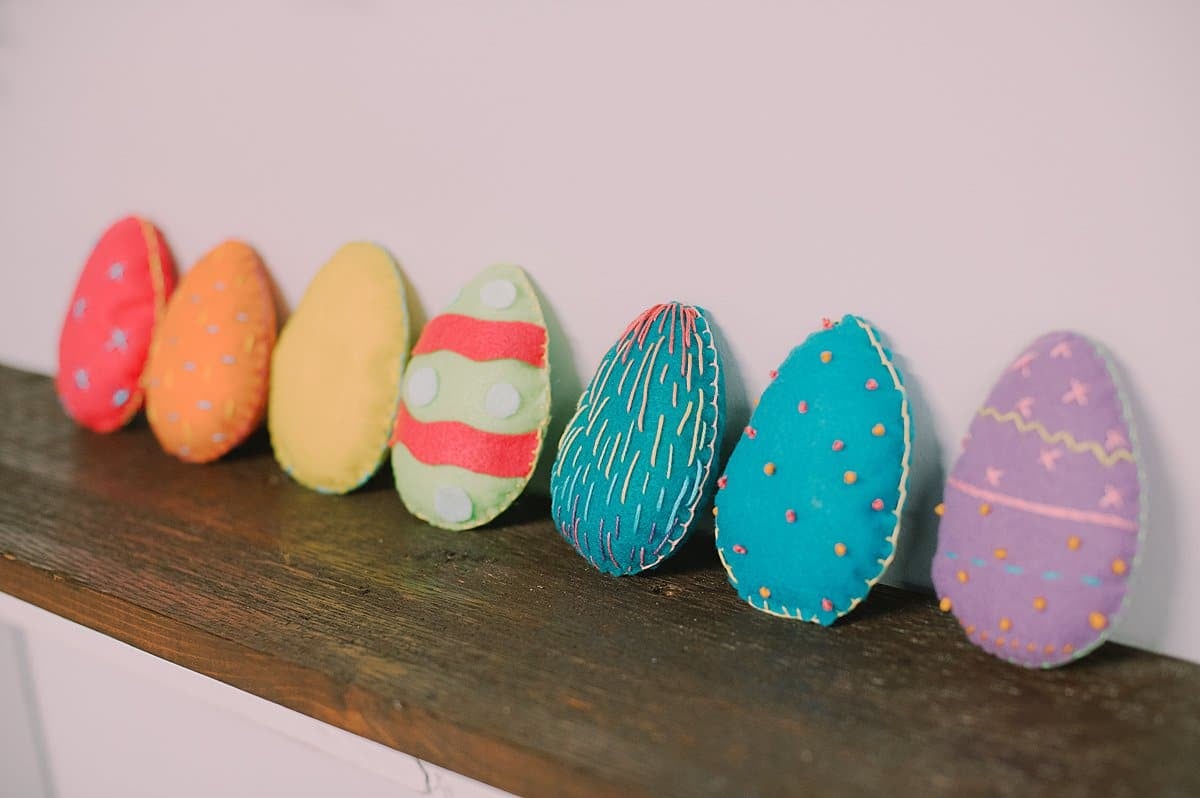 Colorful 3D felt easter eggs lined up on a wood shelf.